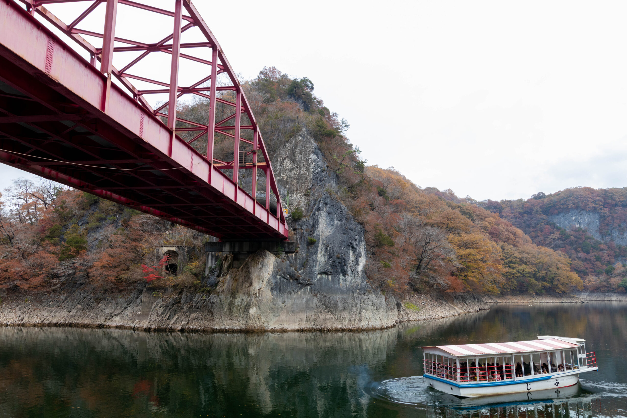 紅葉した帝釈峡・神龍湖の岸と赤い橋、湖上の遊覧船