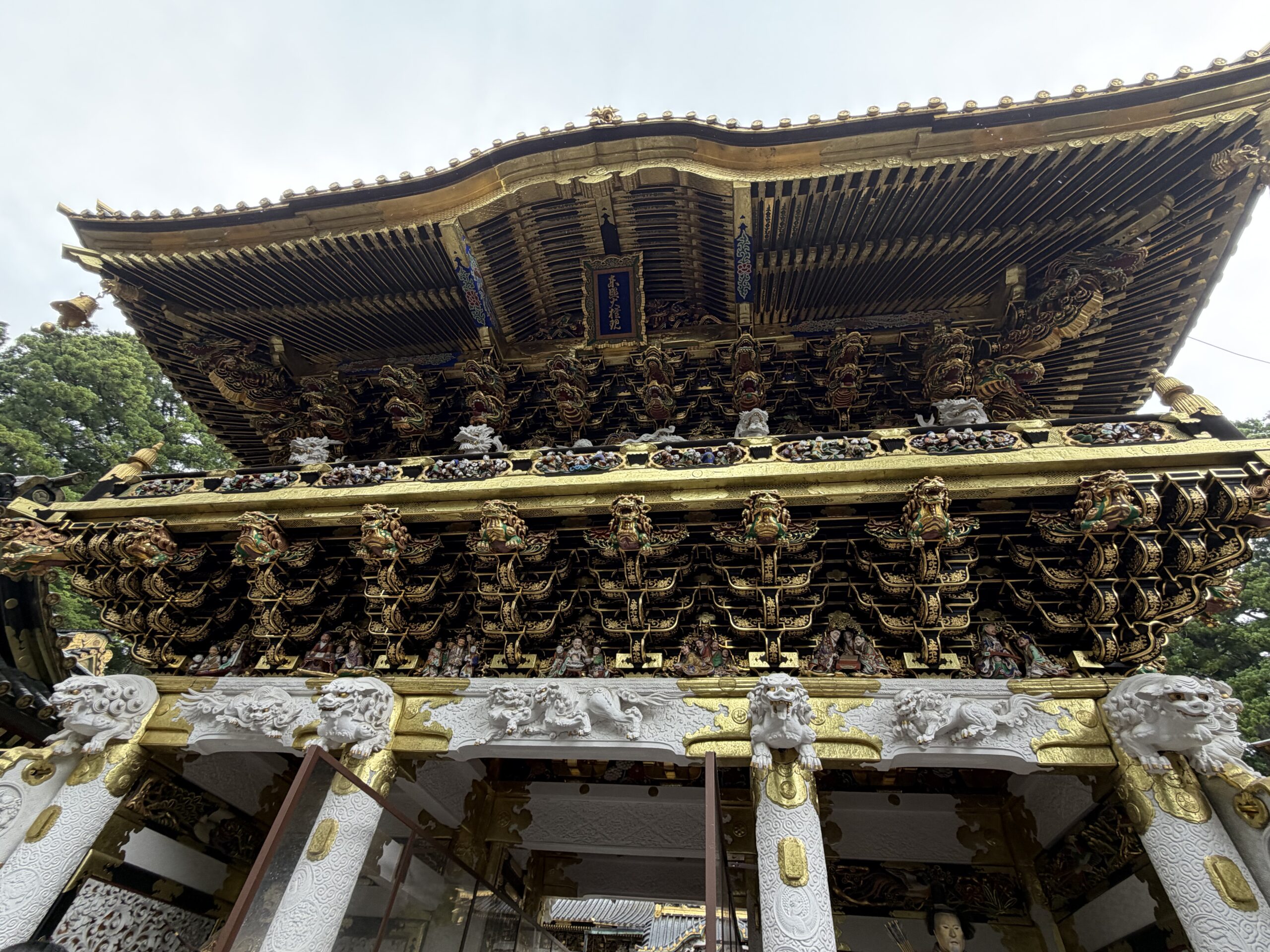 日光東照宮の陽明門を見上げた写真。白と金色の彫刻が重なる