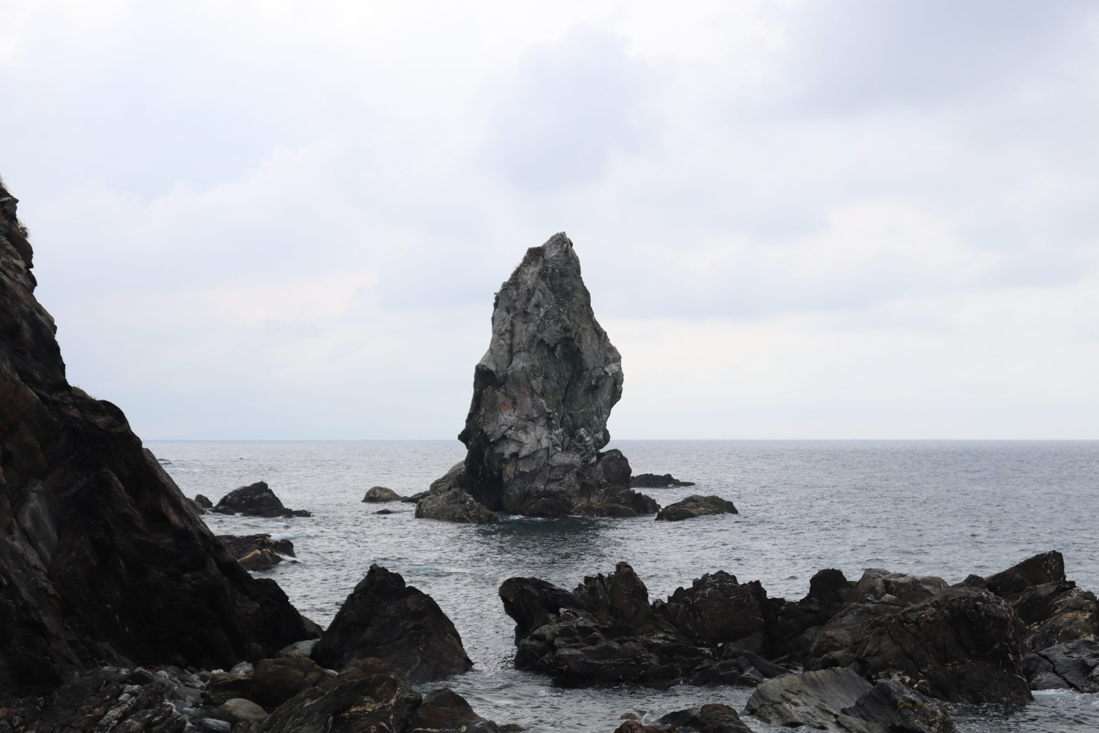 岩場の向こうの海にそびえる沼島の上立神岩