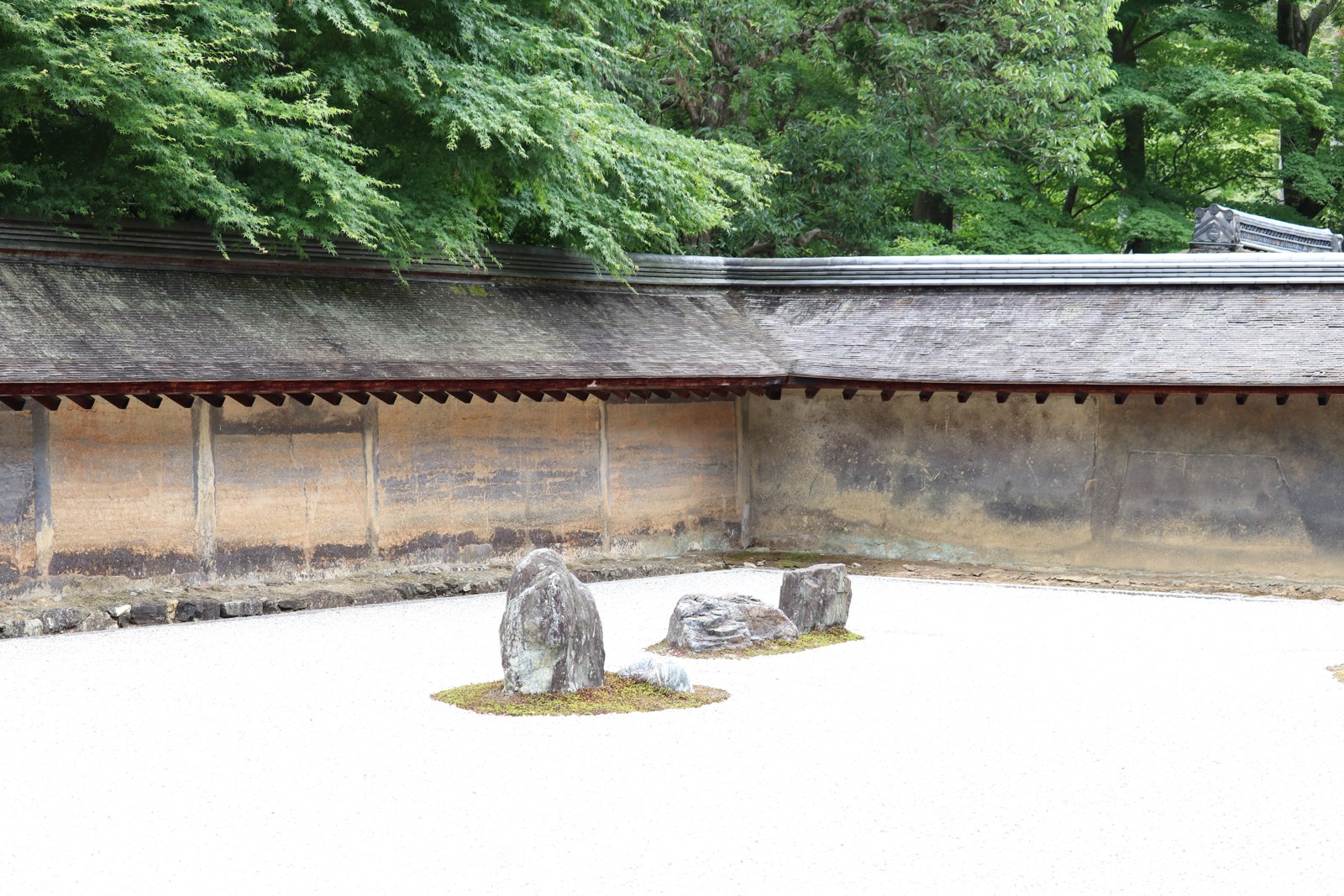 龍安寺の石庭に置かれた石と土塀、奥の木々