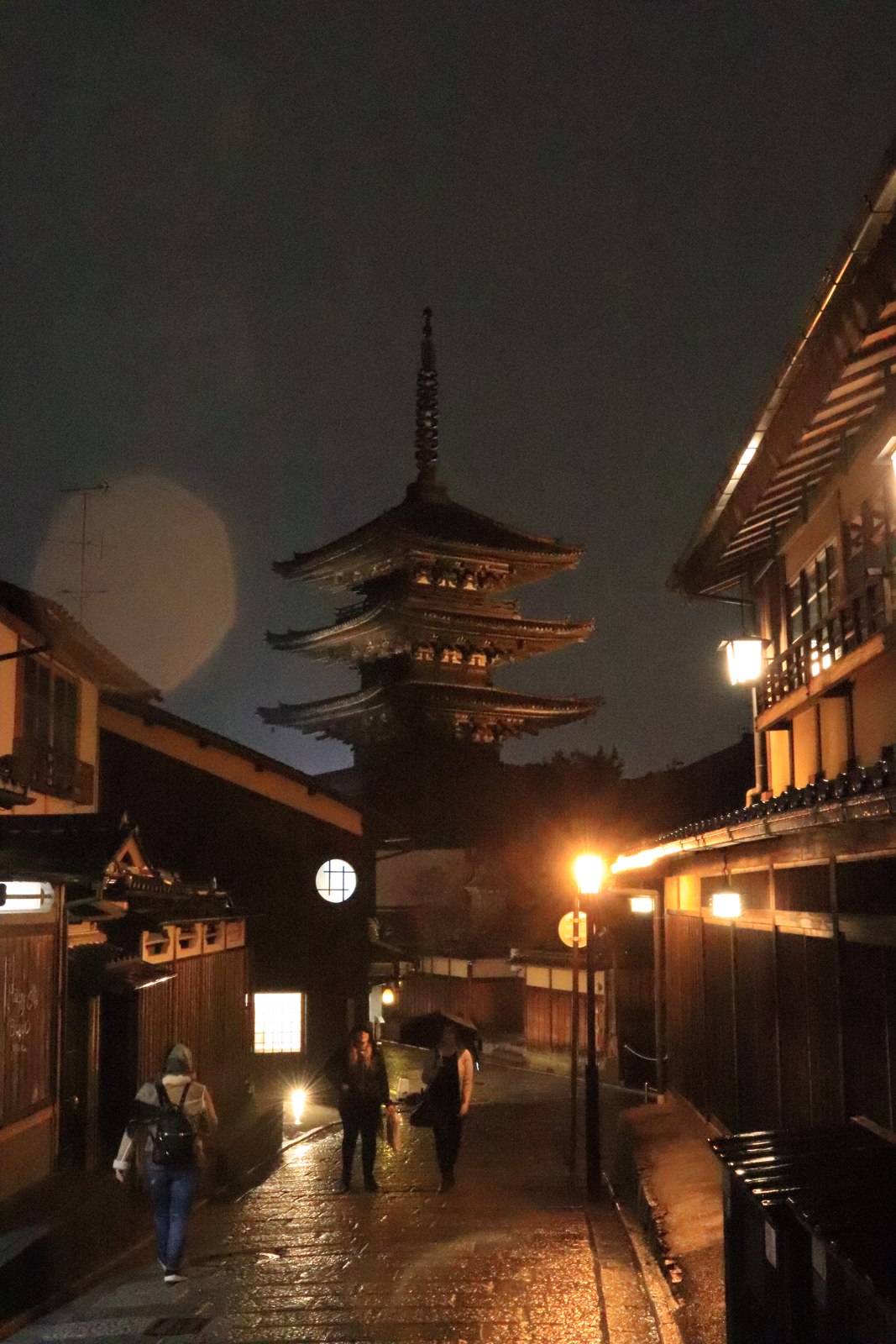 夜の町家の間に見える八坂の塔と灯りが反射する濡れた石畳